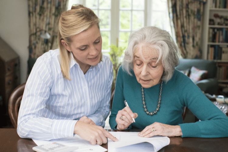 A woman helping an elderly woman with signing documents.